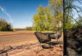 Buitenterras bij ÖÖD Suite Wilsumer Berge, Duitsland, met twee stoelen, tafel en uitzicht op veld en bos.