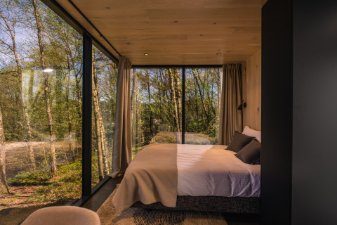 Soveværelse i ÖÖD Suite tiny house ved Wilsumer Berge i Tyskland, med panoramaudsigt over skov.