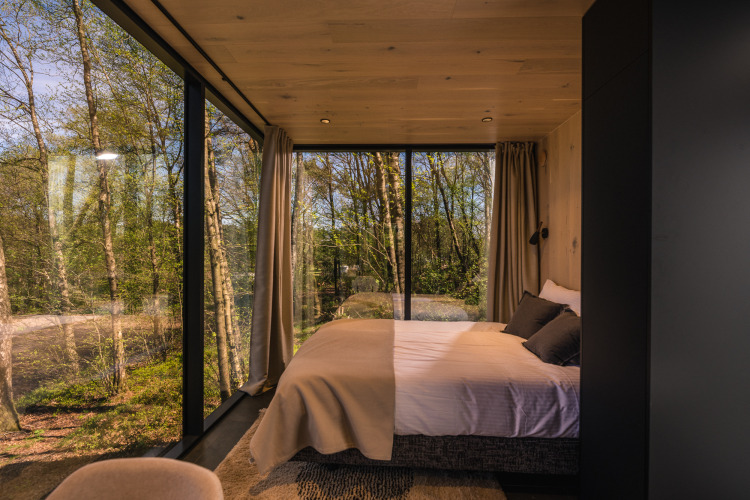 Bedroom in the ÖÖD Suite tiny house at Wilsumer Berge, Germany, with panoramic forest views through glass.