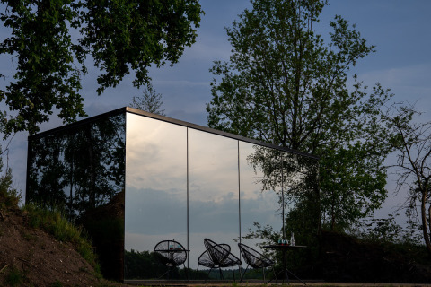 Spiegelende glazen gevel van de ÖÖD Suite tiny house bij Wilsumer Berge in Duitsland, omringd door bomen.