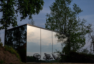 Spiegelende glazen gevel van de ÖÖD Suite tiny house bij Wilsumer Berge in Duitsland, omringd door bomen.