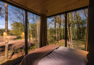 Slaapkamervizier in een tiny house met glaswanden bij ÖÖD Suite, Wilsumer Berge, Duitsland, op het bos.
