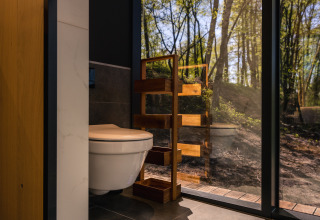 Modernes Badezimmer mit WC und Holzregal, Blick durch Glaswand auf Wald im ÖÖD Suite, Wilsumer Berge.