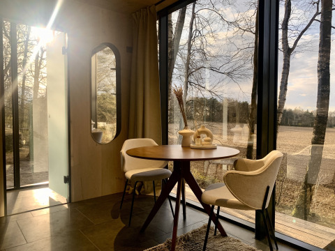 Solrigt interiør i en tiny house ÖÖD Suite med glasvægge og markudsigten ved Wilsumer Berge, Tyskland.