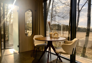 Zonnig interieur van ÖÖD Suite tiny house met glazen wanden en uitzicht op het veld bij Wilsumer Berge, Duitsland.