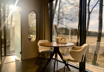 Intérieur ensoleillé d'une tiny house ÖÖD Suite avec murs vitrés et vue sur les champs à Wilsumer Berge, Allemagne.