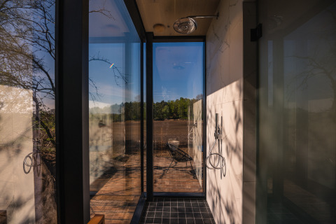 Douche met glazen wanden in ÖÖD Suite op Wilsumer Berge, Duitsland, met uitzicht op terras en natuur.