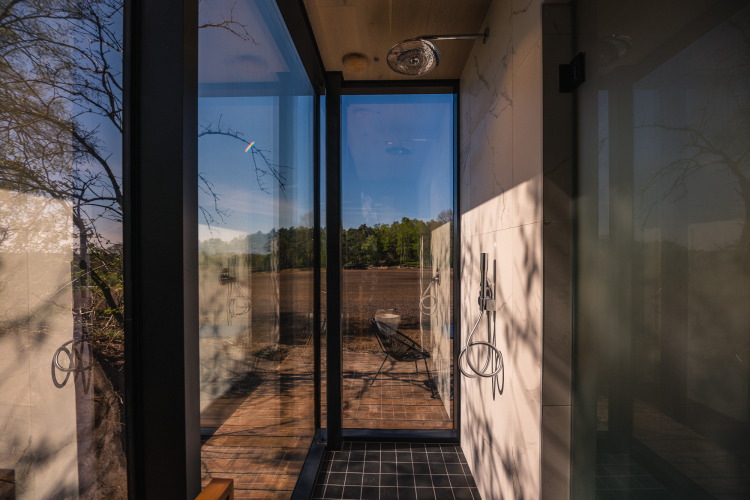 Glass-walled shower in ÖÖD Suite at Wilsumer Berge, Germany, offering a scenic view to the outdoors and terrace.