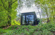 Nokken Forest Cabin: pequeña casa negra con gran ventanal rodeada de bosque verde en Wilsumer Berge, Alemania.
