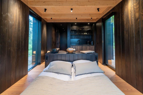 Interiør af Nokken Forest Cabin ved Wilsumer Berge i Tyskland, med seng, store vinduer og køkken.