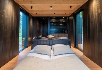 Interiør af Nokken Forest Cabin ved Wilsumer Berge i Tyskland, med seng, store vinduer og køkken.