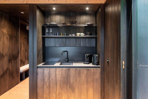 Pequeña cocina moderna en la Nokken Forest Cabin de Wilsumer Berge, Alemania, con madera oscura y estantes.