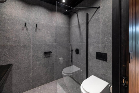 Baño compacto y moderno con azulejos grises, ducha de vidrio y sanitario mural en Nokken Forest Cabin.