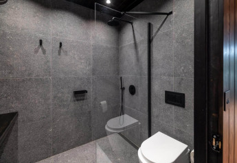 Moderne, kompakt badeværelse med grå fliser, glasbruser og væghængt toilet i Nokken Forest Cabin.