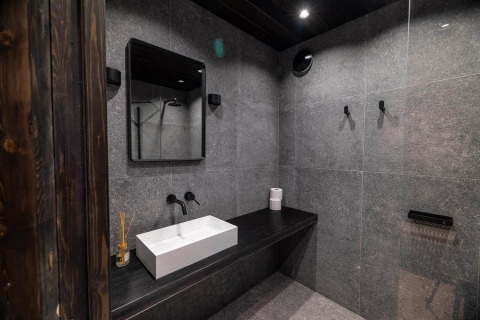 Baño moderno en Nokken Forest Cabin, Wilsumer Berge, Alemania, con azulejos oscuros y lavabo minimalista.