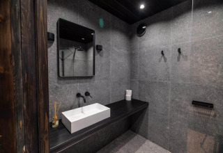 Baño moderno en Nokken Forest Cabin, Wilsumer Berge, Alemania, con azulejos oscuros y lavabo minimalista.