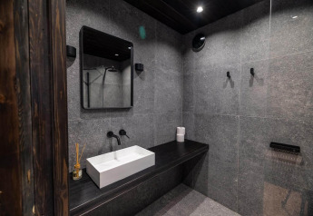 Baño moderno en Nokken Forest Cabin, Wilsumer Berge, Alemania, con azulejos oscuros y lavabo minimalista.