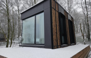 Moderne Nokken NKN-18 tiny house på Wilsumer Berge i Tyskland med sneklædt terrasse og skovbaggrund.