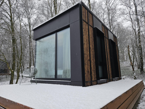 Nokken NKN-18 tiny house at Wilsumer Berge, Germany, with snowy terrace and forest in the background.