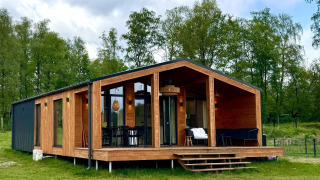 Modern wooden lodge with glass front, The Beach House at Wilsumer Berge in Germany, surrounded by trees.
