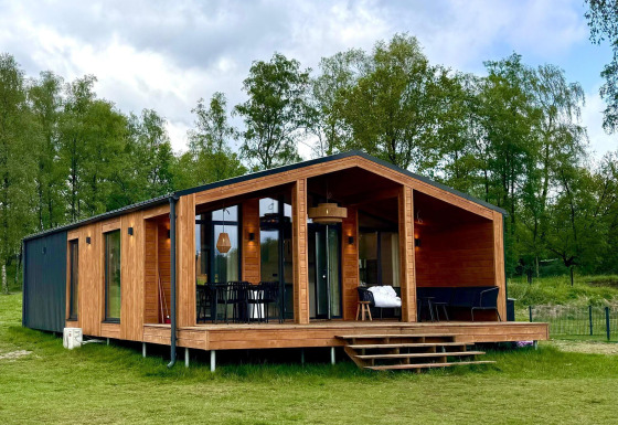 Moderno lodge in legno con facciata in vetro, The Beach House a Wilsumer Berge, Germania, tra alberi.