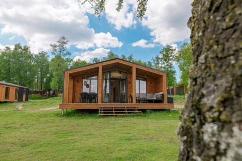 Moderne houten lodge bij The Beach House, Wilsumer Berge, Duitsland, omringd door groen en blauwe lucht.