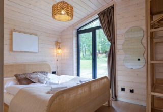Dormitorio de The Beach House en Wilsumer Berge, Alemania, con pared de madera, cama acogedora y puerta acristalada.