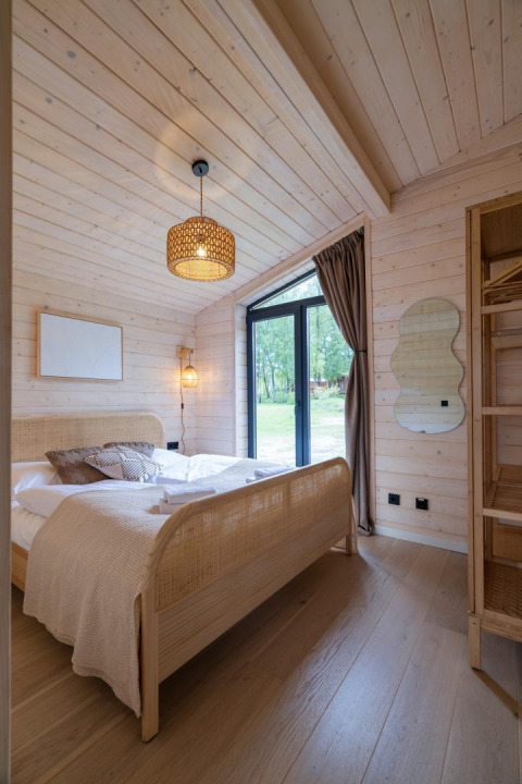 Chambre du lodge The Beach House à Wilsumer Berge, Allemagne, avec bois clair, lit confortable et porte vitrée.