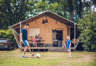 Familia se divierte y juega al fútbol frente a una tienda safari en Veluwepark de Bosgraaf, Países Bajos.