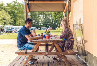 Familia sentada en una mesa de picnic junto a una tienda safari en Veluwepark de Bosgraaf, Países Bajos.