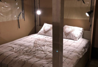 Área de dormitorio en una tienda safari en Veluwepark de Bosgraaf, Países Bajos, con cama doble y luces cálidas.