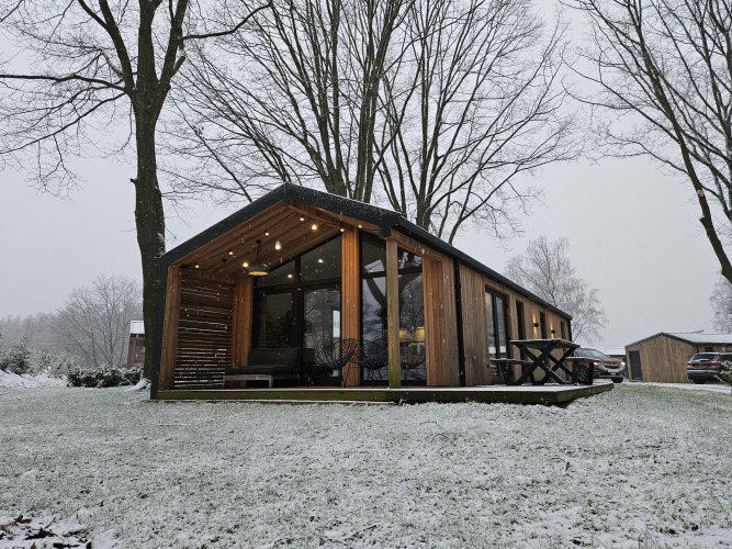Modern wooden cabin at Nature Lodge, Wilsumer Berge, Germany, surrounded by snowy winter trees and lawn.