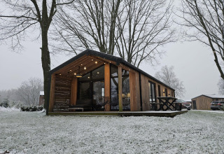 Moderne houten lodge bij Nature Lodge, Wilsumer Berge, Duitsland, omgeven door sneeuw en hoge bomen.