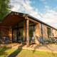 Lodge moderne en bois avec grande terrasse, mobilier extérieur et environnement verdoyant sous un beau ciel.