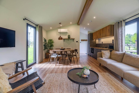 Sala moderna de lodge con grandes ventanas, suelo de madera, muebles acogedores y cocina abierta.