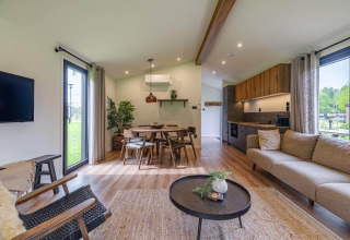 Sala moderna de lodge con grandes ventanas, suelo de madera, muebles acogedores y cocina abierta.