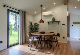Coin repas dans un lodge avec table ronde en bois, six chaises, grandes fenêtres et déco moderne.