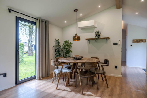 Comedor en una cabaña con mesa redonda de madera, seis sillas, ventanales y decoración moderna.