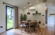 Eethoek in een lodge, met ronde houten tafel, zes stoelen, grote ramen en moderne inrichting.
