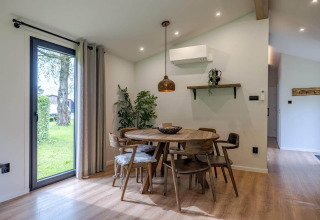 Coin repas dans un lodge avec table ronde en bois, six chaises, grandes fenêtres et déco moderne.