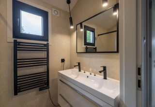Baño moderno en una cabaña con toallero calefactable negro, lavabo doble, gran espejo y luces suaves.