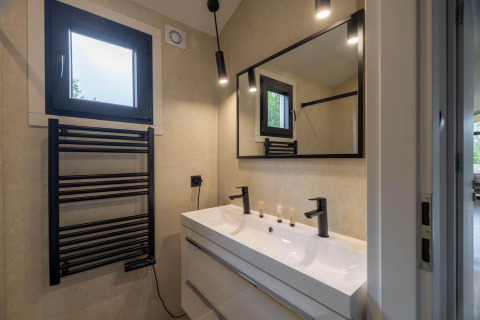 Baño moderno en una cabaña con toallero calefactable negro, lavabo doble, gran espejo y luces suaves.