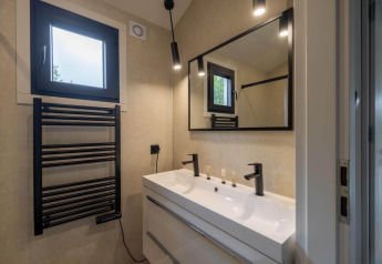 Moderne lodgebadkamer met zwarte handdoekradiator, dubbele wastafel, groot spiegel en zachte verlichting.