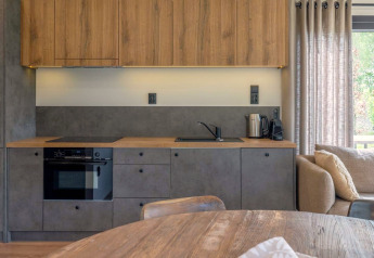 Modern lodge kitchenette with wooden cabinets, gray fronts, oven, kettle, and window with curtains.