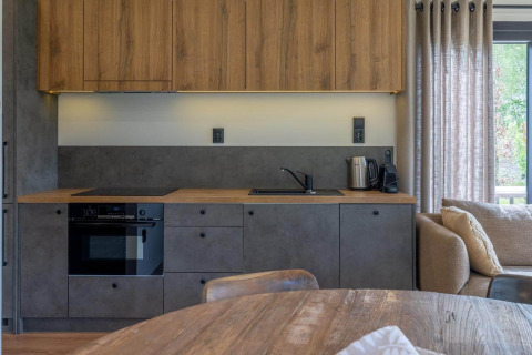Moderne lodgekeuken met houten bovenkasten, grijze onderkasten, oven, waterkoker en gordijnen.