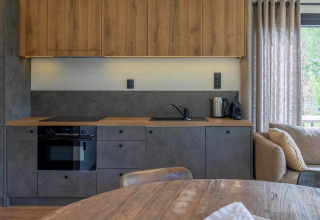 Modern lodge kitchenette with wooden cabinets, gray fronts, oven, kettle, and window with curtains.
