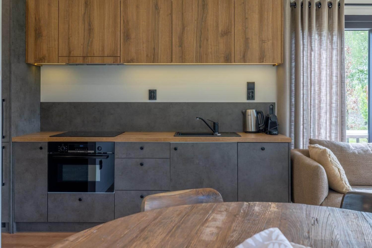 Modern lodge kitchenette with wooden cabinets, gray fronts, oven, kettle, and window with curtains.