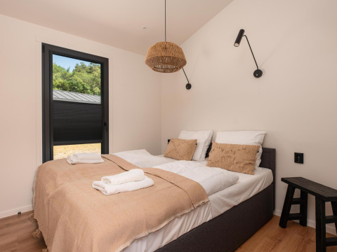 Moderne lodge-slaapkamer met een tweepersoonsbed, beige deken, kussens en een raam met natuuraanzicht.