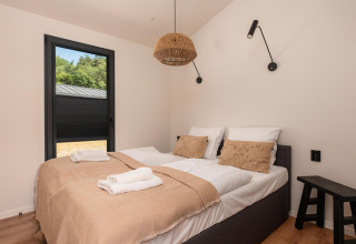 Dormitorio moderno en una cabaña con cama doble, manta beige, almohadas y ventana con vista al exterior.