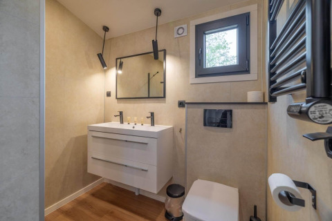 Salle de bain moderne dans un lodge avec double vasque, miroir carré, fenêtre, WC et éclairages design.